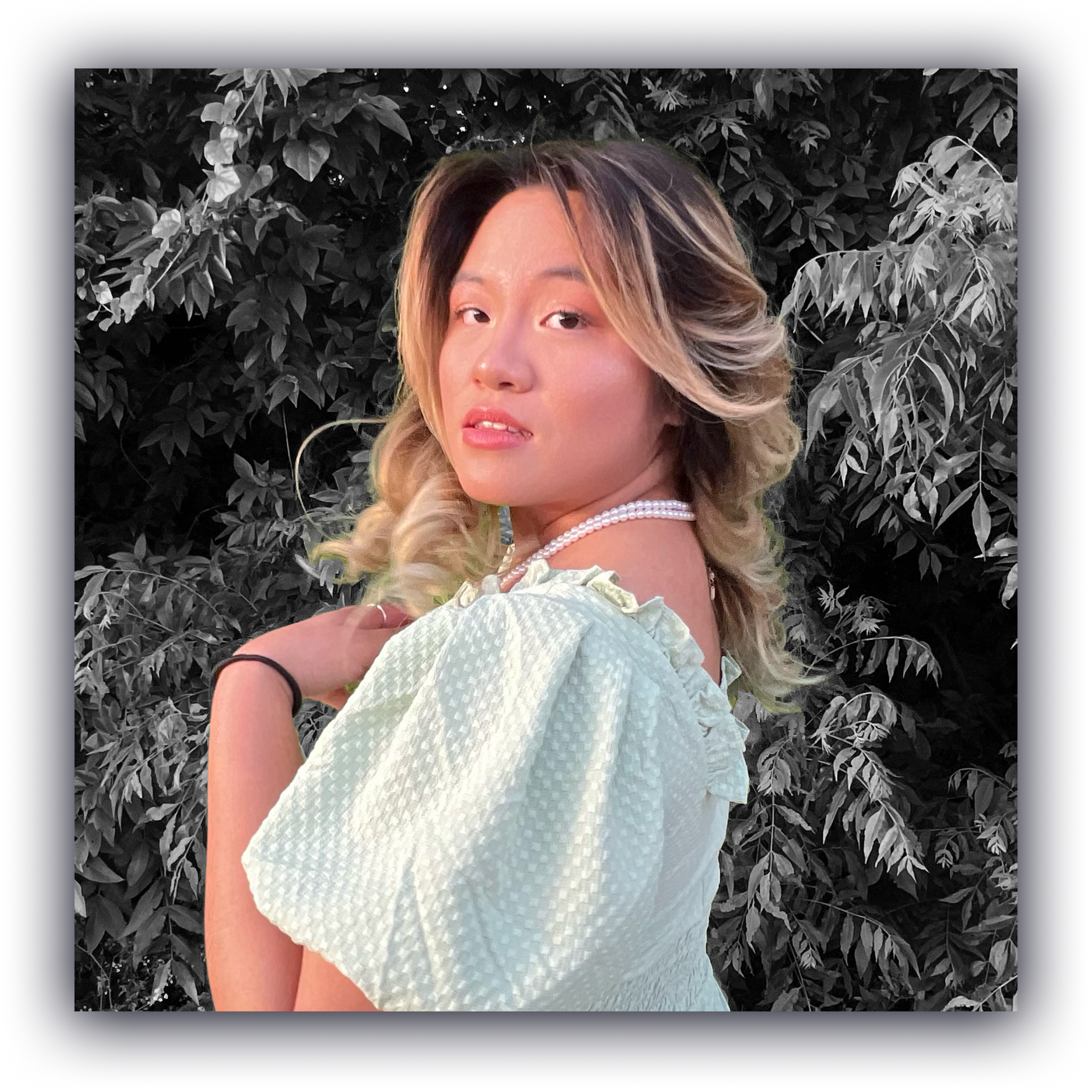 A picture of Emily Nguyen with blonde hair in front of a forest while wearing a pastel sage green dress.